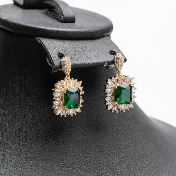 Paire de boucles d'oreilles pendantes de la marque Ascellà Algérie avec des pierres emerald green et un entourage de cristaux scintillants sur support doré.