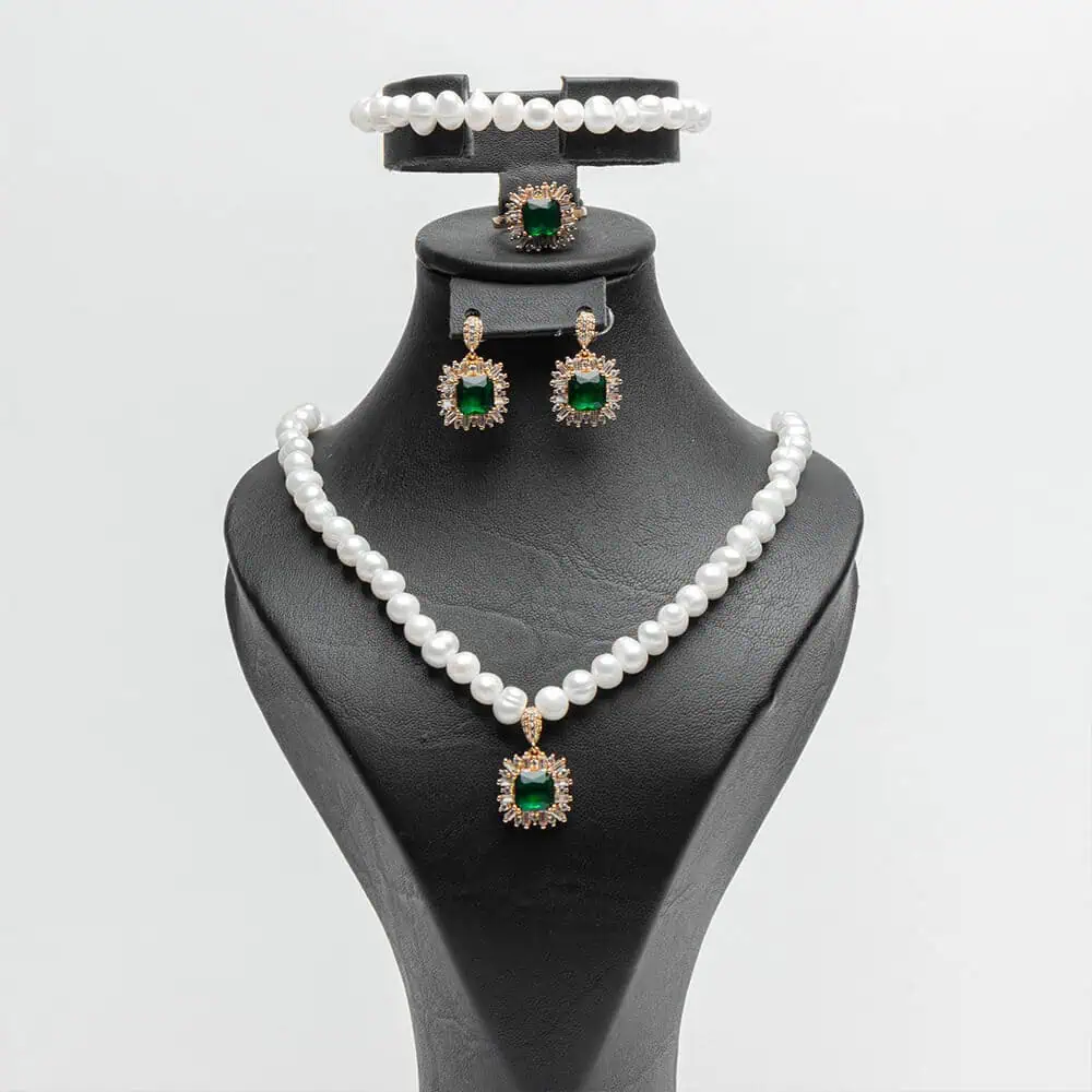 une parure de bijoux de la marque Ascellà Algérie comprenant un collier et un bracelet en perles d'eau douce, des boucles d'oreilles et une bague assorties avec des pierres emerald vert.