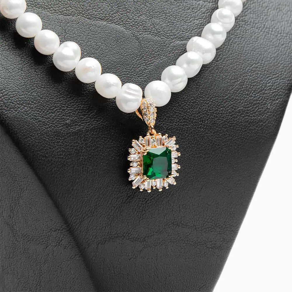 Détail d'un collier Ascellà Algérie en perles d'eau douce blanches avec un pendentif rectangulaire de couleur emerald green entouré de cristaux clairs.